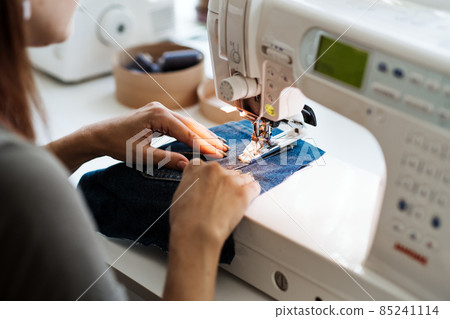 Reuse, repair, upcycle. Denim upcycling ideas, repair and using old jeans. Close-up of sewing machine with shabby, old, torn denim jeans fabric. Sewing studio working process. Reuse, repair, upcycle. Denim upcycling ideas, repair and using old jeans. Close-up of sewing machine with shabby, old, torn denim jeans fabric. Sewing studio working process. 85241114