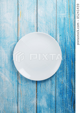 An empty round white plate on a blue wooden table. An empty round white plate on a blue wooden table. 85241439
