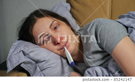 Woman catches cold and measures temperature lying on sofa 85242147