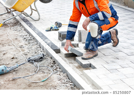 A worker lays down paving slabs with a rubber hammer on a pedestrian stretch of sidewalk. Vertical image. 85250807