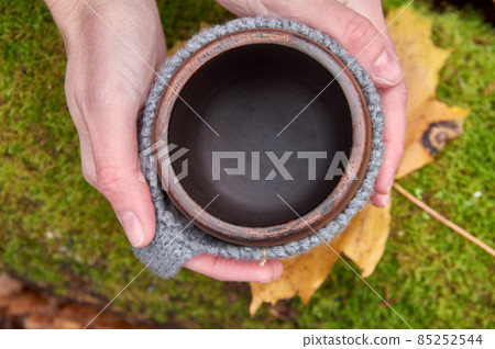 Empty mug in women's hands. View from above against the background of green moss. Picnic, hike, cozy. Empty mug in women's hands. View from above against the background of green moss. Picnic, hike, cozy. 85252544