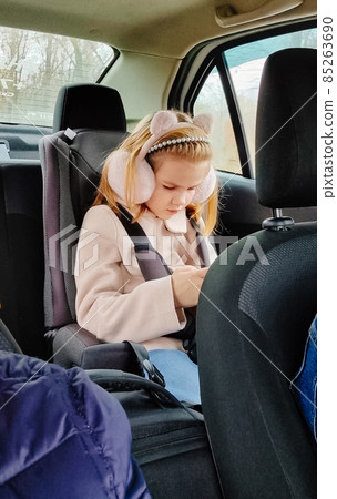 a little girl sits in a car seat and plays on her phone. a little girl sits in a car seat and plays on her phone. 85263690