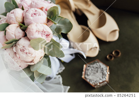 Wedding bouquet of white peonies, shoes and wedding rings on a wooden background 85264251
