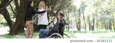 Disabled man in wheelchair giving five to female friends in park 85265213