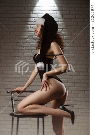 A woman in a red Santa hat with Christmas gifts on the floor poses sexually with a white background A woman in a red Santa hat with Christmas gifts on the floor poses sexually with a white background 85265974