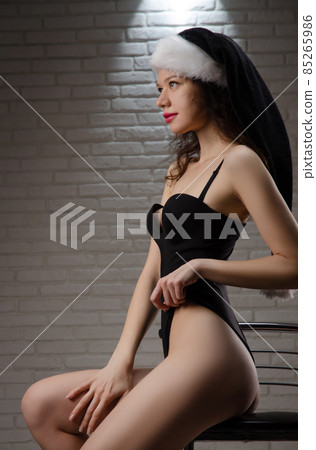 A woman in a black Santa hat in a sexy bodysuit on a bar stool 85265986