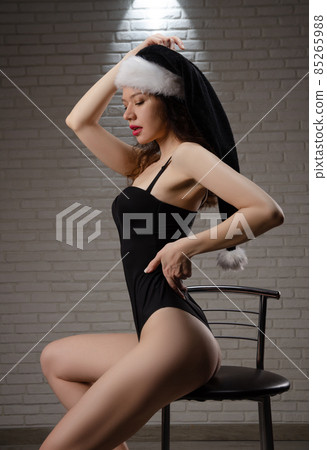 A woman in a black Santa hat in a sexy bodysuit on a bar stool 85265988