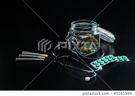 Dry medical cannabis in a jar with a stethoscope on a black background Dry medical cannabis in a jar with a stethoscope on a black background 85265994