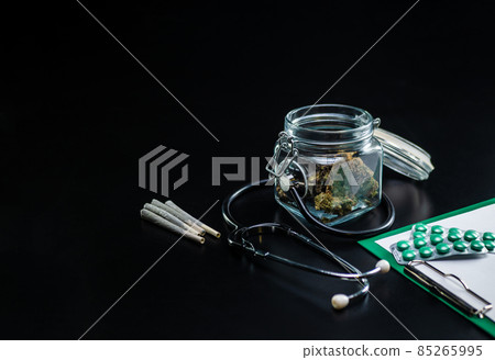 Dry medical cannabis in a jar with a stethoscope on a black background Dry medical cannabis in a jar with a stethoscope on a black background 85265995