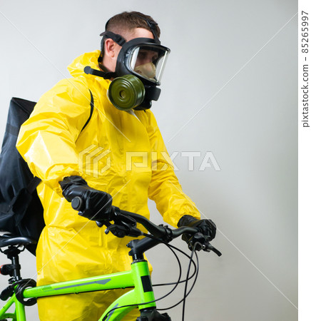 a courier delivering food on a bicycle wearing a gas mask and a protective yellow suit a courier delivering food on a bicycle wearing a gas mask and a protective yellow suit 85265997