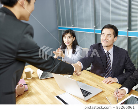 two asian corporate executives shaking hands during meeting in office 85266061