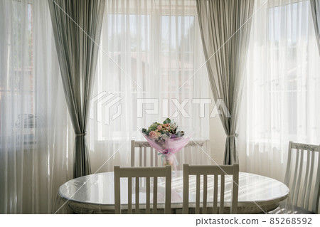 white oval table with a bouquet of flowers in a room with large windows.  85268592