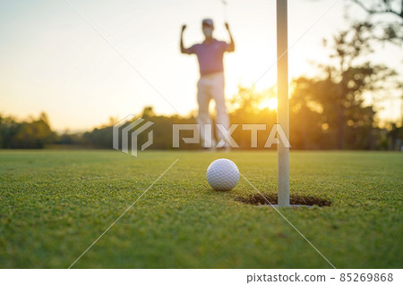 Golfer action to win after long putting golf ball on the green golf, lens flare on sun set evening time. Golfer action to win after long putting golf ball on the green golf, lens flare on sun set evening time. 85269868