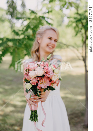 Bride with flowers outdoors. Portrait of a beautiful bride in a long white wedding dress with a bouquet of flowers in a forest park. Beautiful bride in fashion wedding dress on natural background.The 85271714
