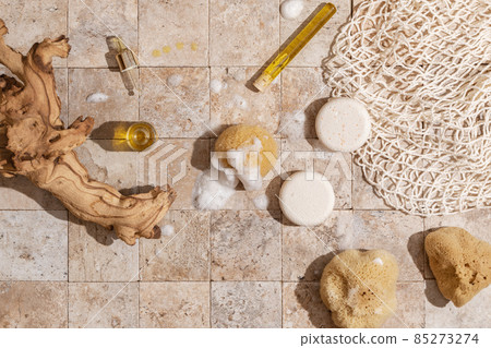 Zero waste bathroom accessories - soap, dry shampoo, natural sea sponge with organic soap foam, wood brush, skin oil, mesh bag on earth toned stone tales top view direct sunlight 85273274