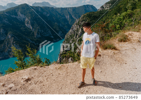 Guy traveler on the background The famous Piva Canyon with its fantastic reservoir. View of road above Piva Lake (Pivsko Jezero) in Montenegro. man looks at river Piva, Montenegro. 85273649