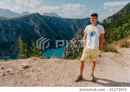 Guy traveler on the background The famous Piva Canyon with its fantastic reservoir. View of road above Piva Lake (Pivsko Jezero) in Montenegro. man looks at river Piva, Montenegro. 85273652