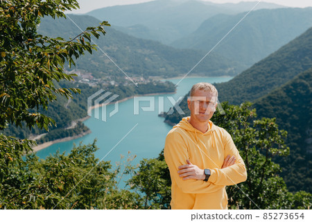 Man - Traveler on the background The famous Piva Canyon with its fantastic reservoir. View of road above Piva Lake (Pivsko Jezero) in Montenegro. man looks at river Piva, Montenegro. 85273654