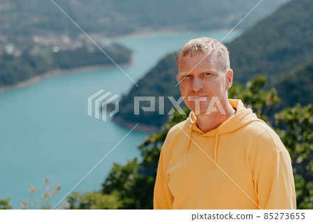 Man - Traveler on the background The famous Piva Canyon with its fantastic reservoir. View of road above Piva Lake (Pivsko Jezero) in Montenegro. man looks at river Piva, Montenegro. 85273655