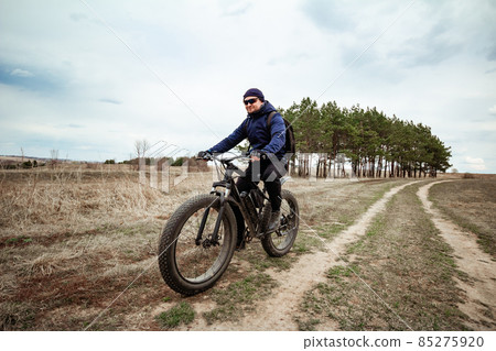 A man rides a fat bike on the road. Rural area. A man rides a fat bike on the road. Rural area. 85275920