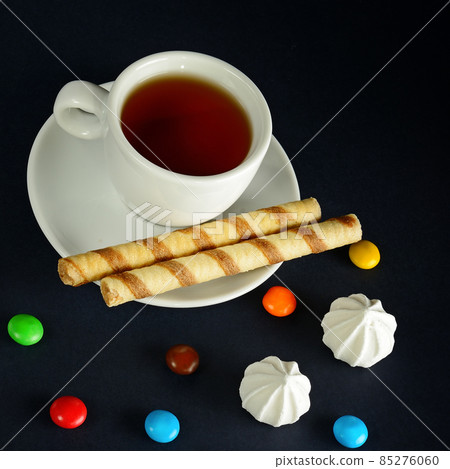 Tea cup and sweets on a black background. 85276060