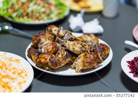 Chicken shanks, chicken legs are served on a plate with various salad plates in the background Chicken shanks, chicken legs are served on a plate with various salad plates in the background 85277142