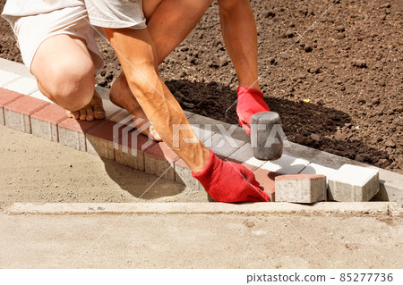 A worker puts paving slabs on the sidewalk on a bright sunny day. A worker puts paving slabs on the sidewalk on a bright sunny day. 85277736