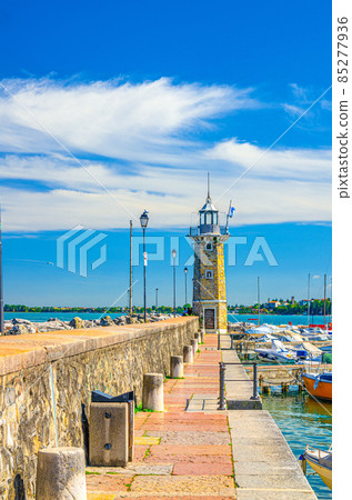 Stone pier mole with lighthouse, street lights and yachts on boat parking port marina in Desenzano del Garda 85277936