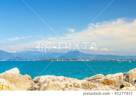 View from stone pier mole of Garda Lake azure water with Monte Baldo mountain range and Sirmione peninsula 85277937