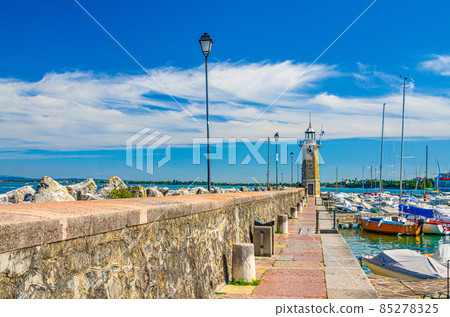 Stone pier mole with lighthouse, street lights and yachts on boat parking port marina in Desenzano del Garda 85278325