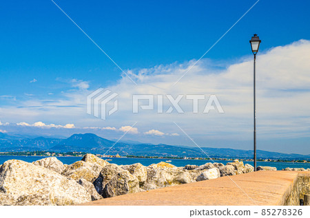 View from stone pier mole of Garda Lake water with Monte Baldo mountain range and Sirmione peninsula 85278326
