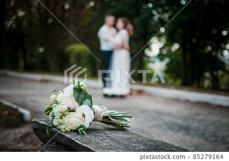 Bouquet of flowers on the front focus and pair of newlyweds on back focus 85279164