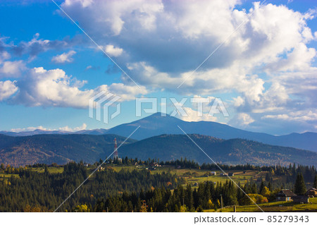 Beautiful mountain scenery with blue sky, white low clouds in a sky at sunny day in spring, summer or fall. A mountain top on a horizon and green coniferous forest. Ukrainian Carpathians landscape. 85279343