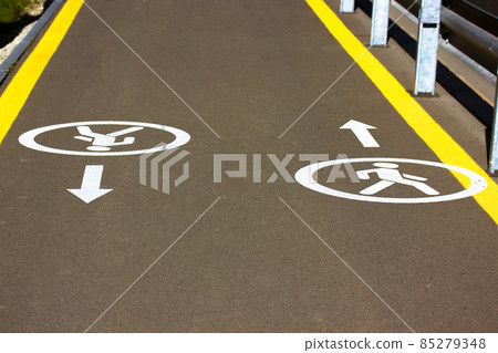 An asphalt road for pedestrians with directional arrows pointing in different directions for easy safe walk. Yellow socket on road. Walk way on a city street. Urban infrastructure. Pedestrian zone. An asphalt road for pedestrians with directional arrows pointing in different directions for easy safe walk. Yellow socket on road. Walk way on a city street. Urban infrastructure. Pedestrian zone. 85279348