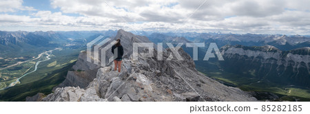 Wide panoramic shot of female hiker enjoying the views on valley from mountain summit 85282185
