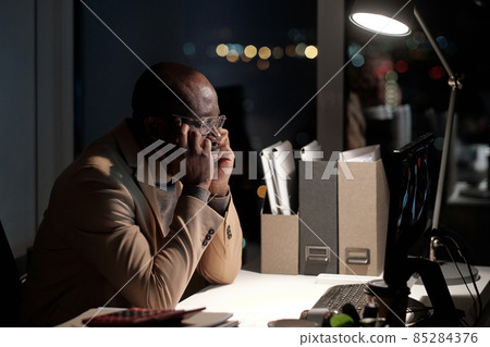Sleepy African businessman touching his face while sitting in front of computer 85284376