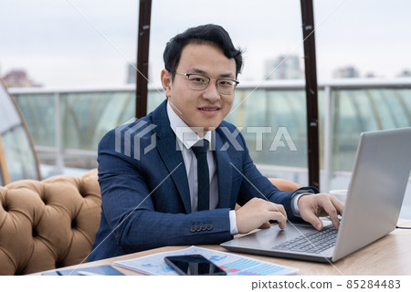 Happy young Chinese businessman in formalwear working in front of laptop Happy young Chinese businessman in formalwear working in front of laptop 85284483