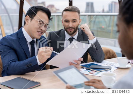 Young successful Asian businessman showing contract to his partner and explaining its terms Young successful Asian businessman showing contract to his partner and explaining its terms 85284485