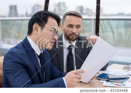 Young Chinese broker showing his Caucasian colleague new contract 85284486