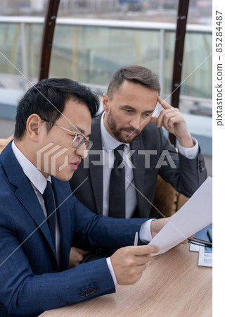 Two confident brokers in formalwear discussing financial paper Two confident brokers in formalwear discussing financial paper 85284487