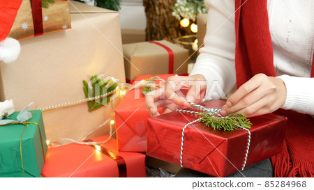 Close up woman hands wrap present gift in cozy living room. Woman wrapping christmas gift box under xmas tree. Asian woman decor bauble ball christmas tree in xmas holiday winter seasonal celebration Close up woman hands wrap present gift in cozy living room. Woman wrapping christmas gift box under xmas tree. Asian woman decor bauble ball christmas tree in xmas holiday winter seasonal celebration 85284968
