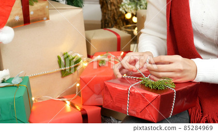 Close up woman hands wrap present gift in cozy living room. Woman wrapping christmas gift box under xmas tree. Asian woman decor bauble ball christmas tree in xmas holiday winter seasonal celebration Close up woman hands wrap present gift in cozy living room. Woman wrapping christmas gift box under xmas tree. Asian woman decor bauble ball christmas tree in xmas holiday winter seasonal celebration 85284969