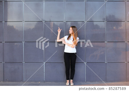 Young energetic female girl raised arms and points to advertising space, worth exactly in full growth on background of wall of business center. Young energetic female girl raised arms and points to advertising space, worth exactly in full growth on background of wall of business center. 85287589