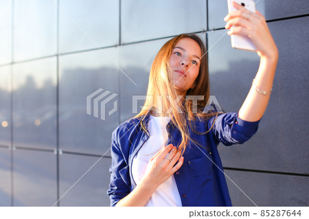 Charming cute girl photographed, makes selfie photos and smiling at camera on outdoors. Charming cute girl photographed, makes selfie photos and smiling at camera on outdoors. 85287644