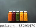 Fresh juices or cocktails of fruits and vegetables in bottles on a gray background.  85293470