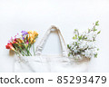 Multicolored freesia flowers and a sprig of cherry blossom in a white canvas bag on a white background 85293479