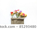 Multicolored freesia flowers and a sprig of cherry blossom in a canvas bag on a white background 85293480