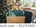 A young beautiful European woman uses her laptop at home in a Christmas festive atmosphere.  85293482