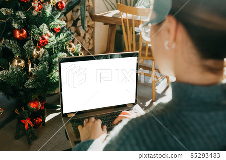 A young beautiful European woman uses her laptop in a Christmas festive atmosphere. Place for text, close-up screen A young beautiful European woman uses her laptop in a Christmas festive atmosphere. Place for text, close-up screen 85293483