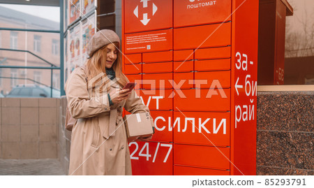 Young caucasian woman picks up mail from automated self-service post terminal machine after online shopping 85293791